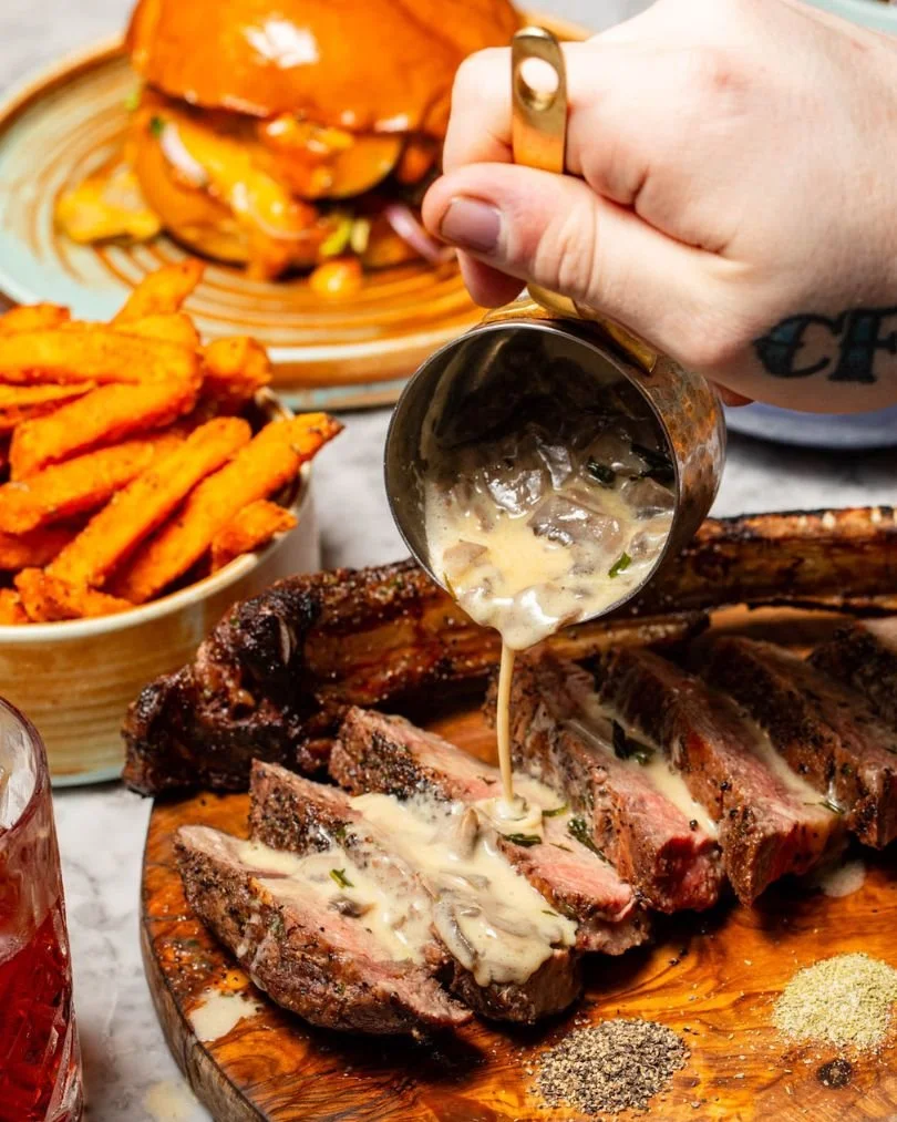 Large steak cut on a wooden platter  has mushroom sauce poured over it.