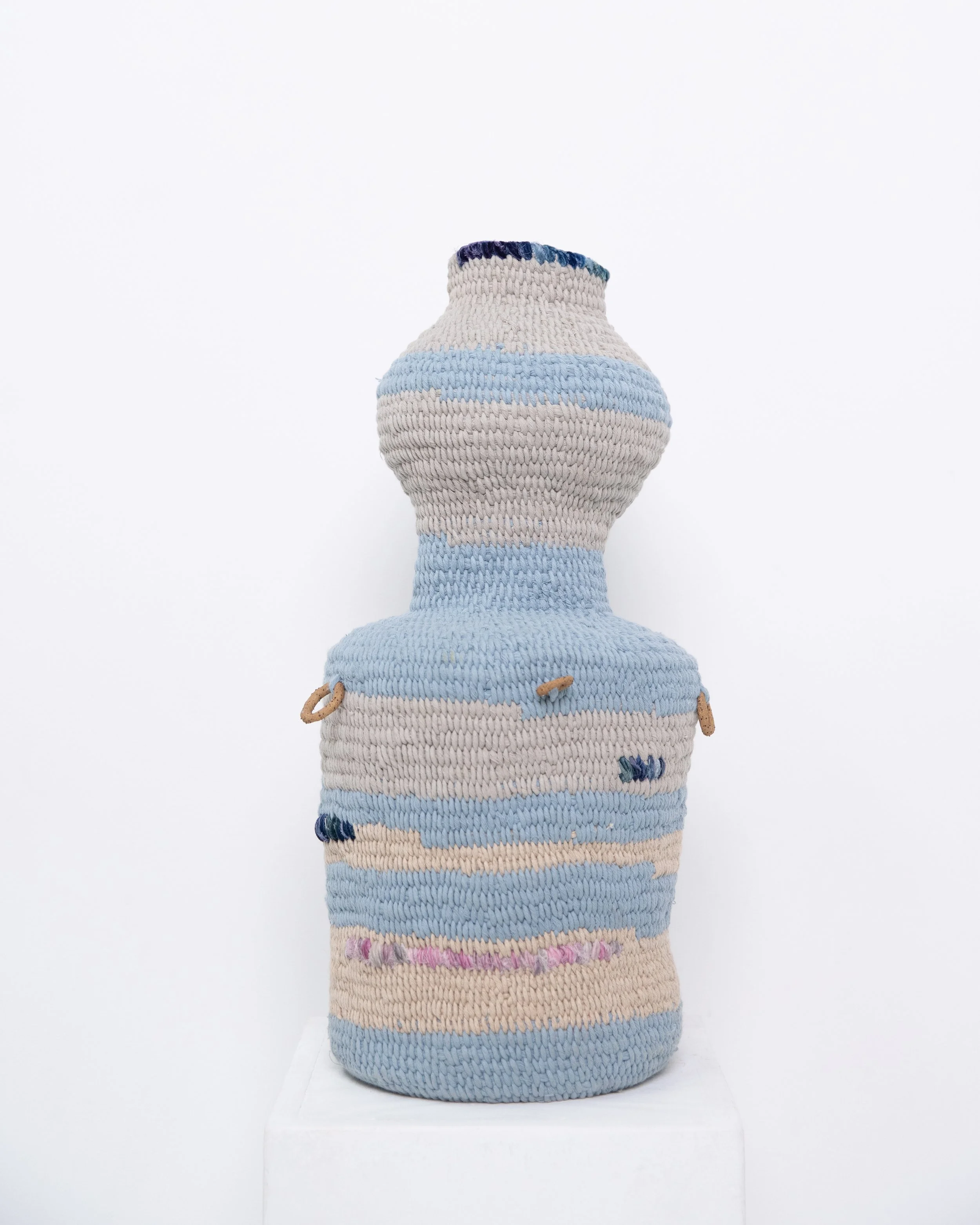 A handwoven textile piece with horizontal stripes in shades of blue, beige, and pink displayed on a white background