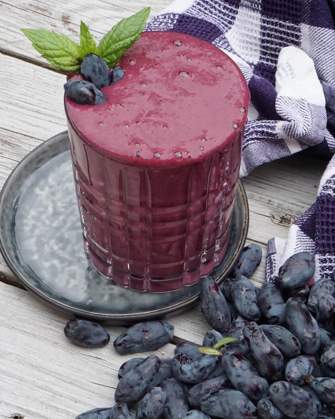 A glass of deep purple honeyberry smoothie with honeyberries on top and around the glass
