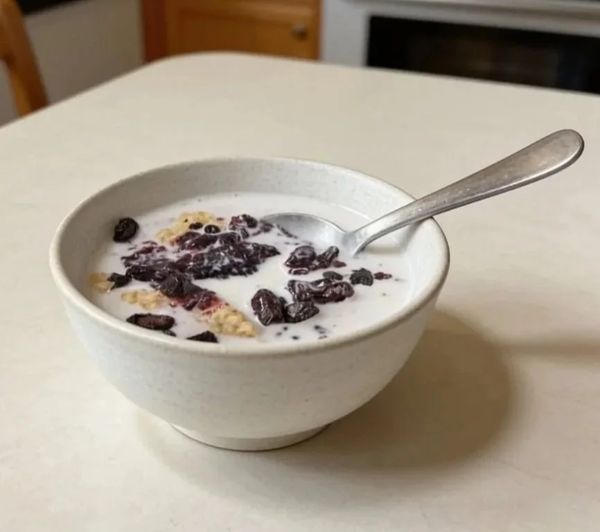 A bowl of cereal with milk and honeyberries on a table, with a spoon inside.