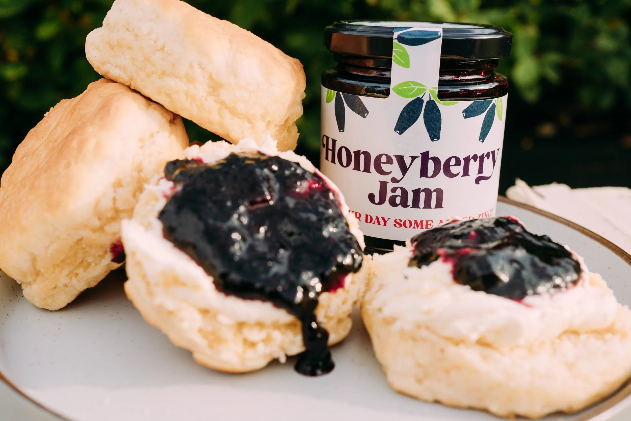 Scones topped with honeyberry jam on a white plate, with a jar of honeyberry jam nearby.