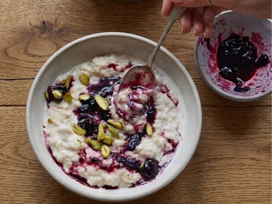 A bowl of porridge with honeyberries and pistachio nuts, with a bowl of honeyberry jam nearby