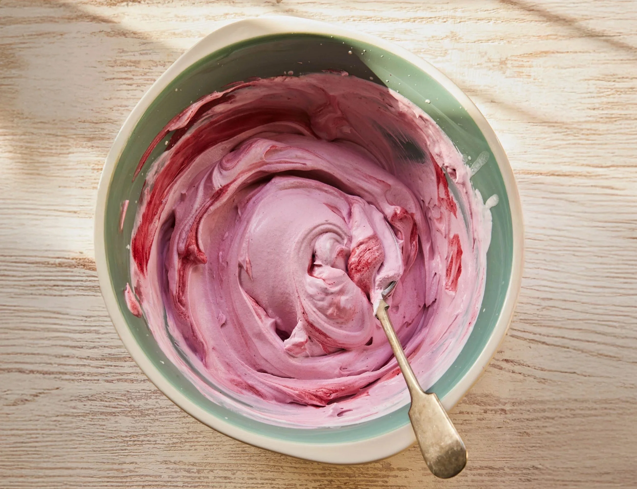 A bowl of yoghurt swirled with honeyberries with a spoon resting inside