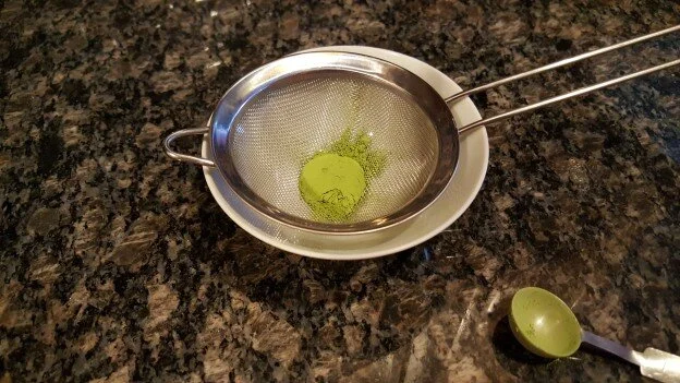 Matcha tea powder, being sifted into a bowl