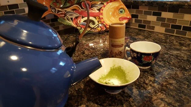 Blue tea kettle, about to pour hot water into cup with Matcha powder in it.
