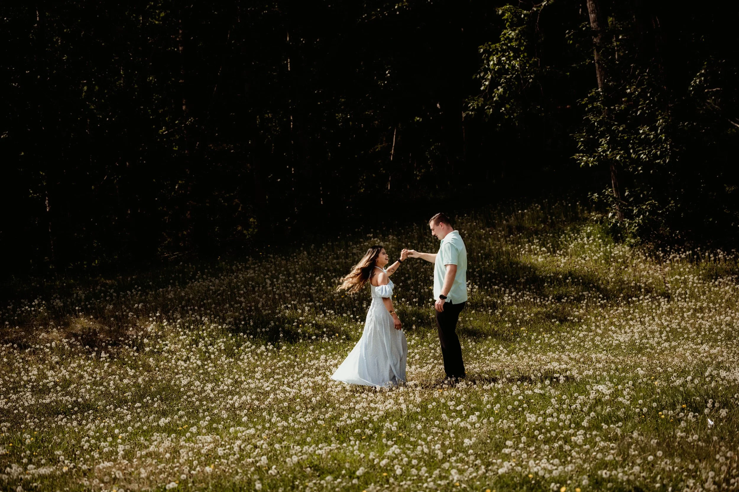 A couple dances in a field of white flowers, with a background of trees.