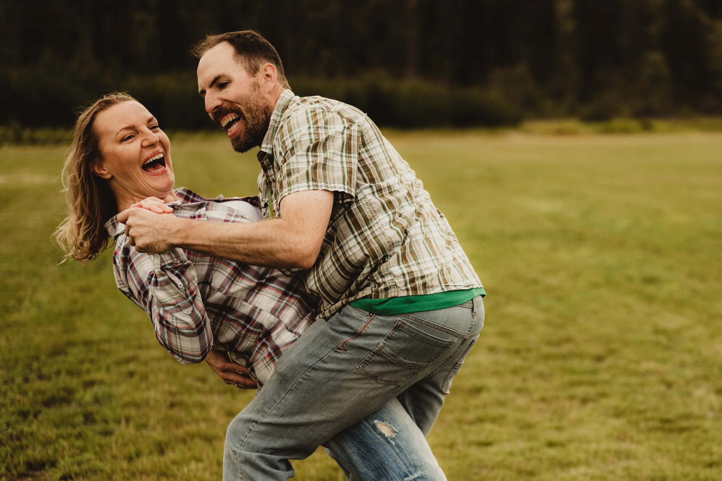 A man and woman playfully wrestling and laughing outdoors on a grassy field.