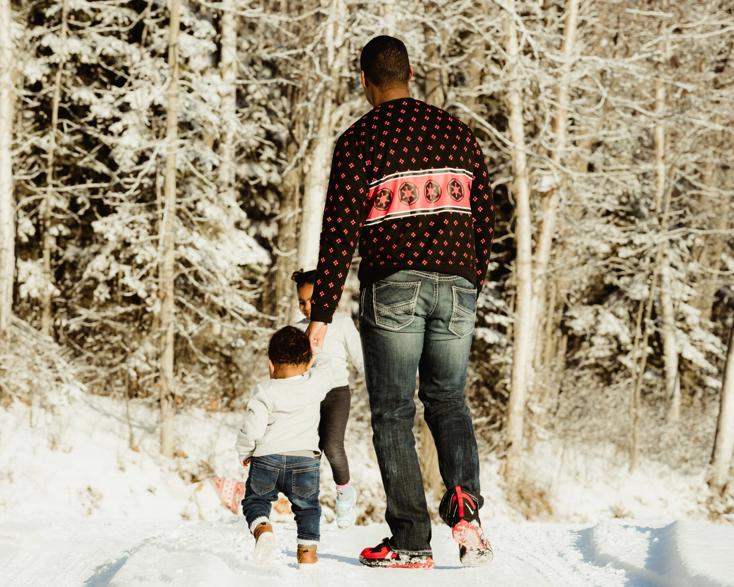 A man and two children walking in a snowy forest, with trees covered in snow in the background.