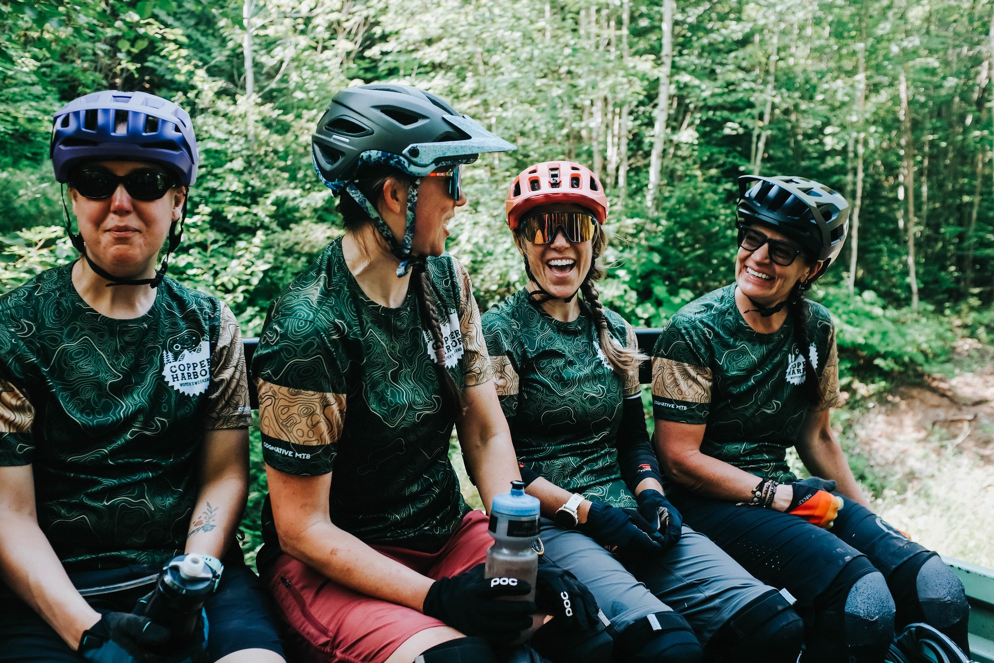 Three women wearing mountain biking gear smile and laugh.