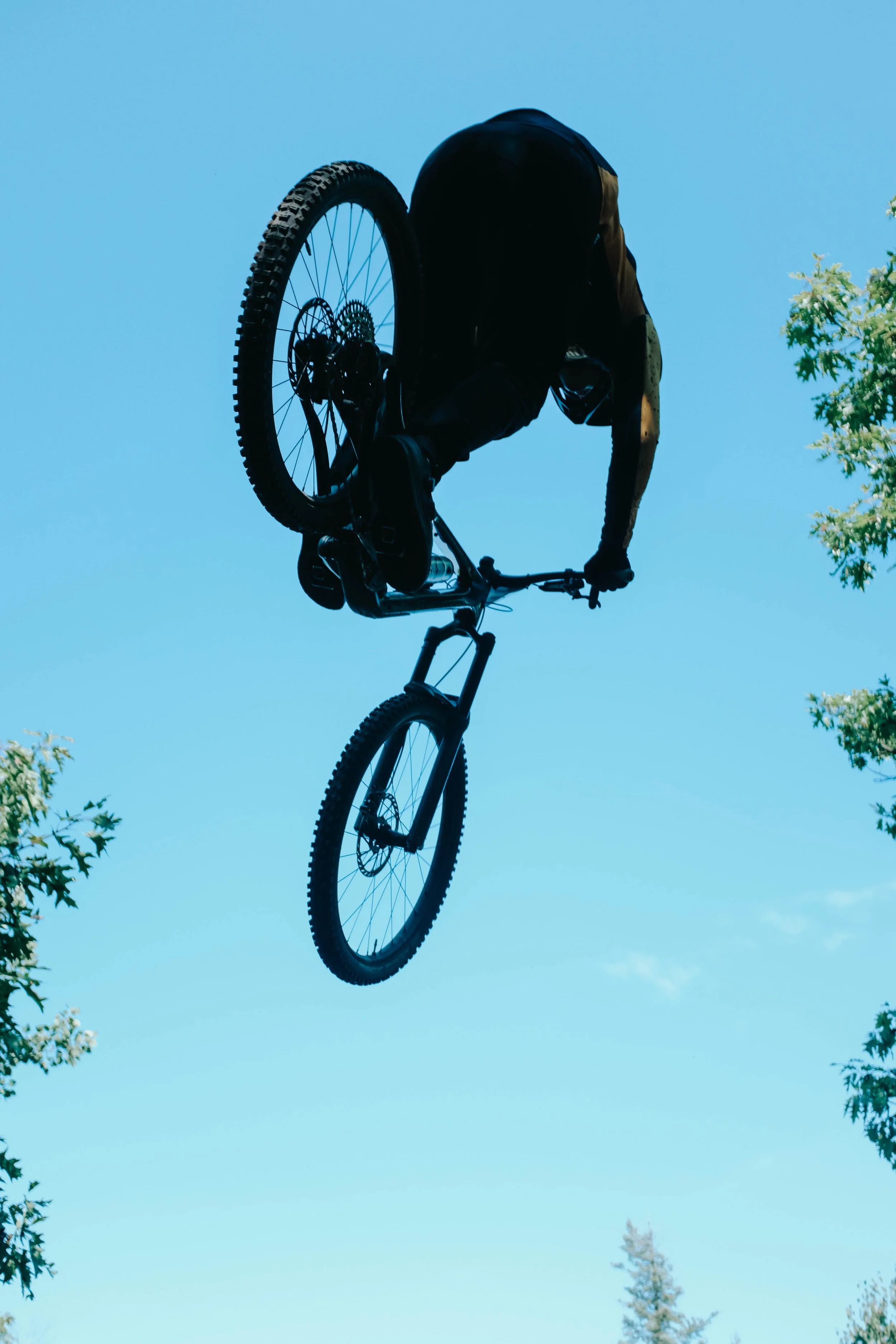 Mountain biker flies through silhouetted in the air with a blue sky in the background.