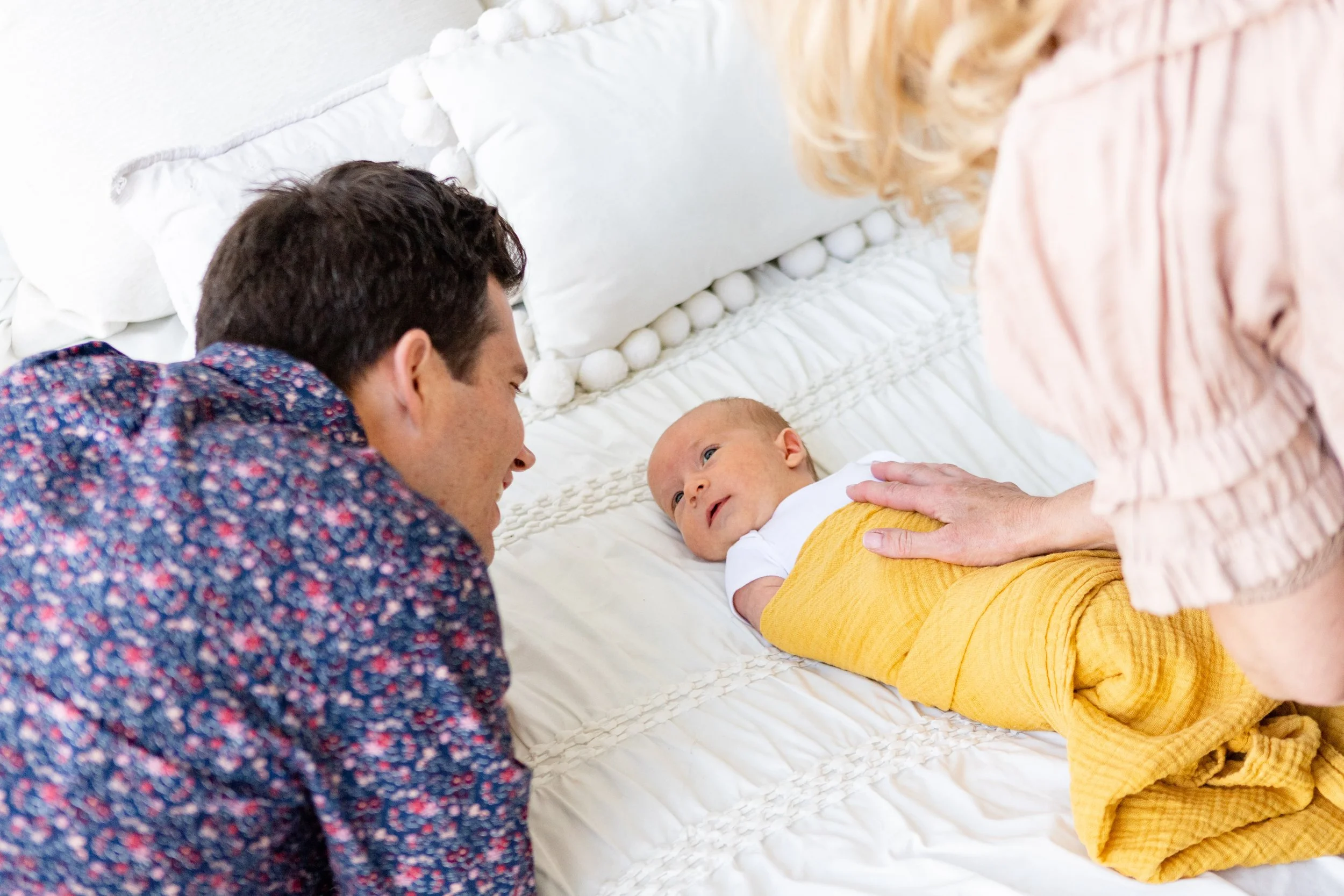 A father and his family assistant and doula in Salt Lake City, Utah play with a newborn.