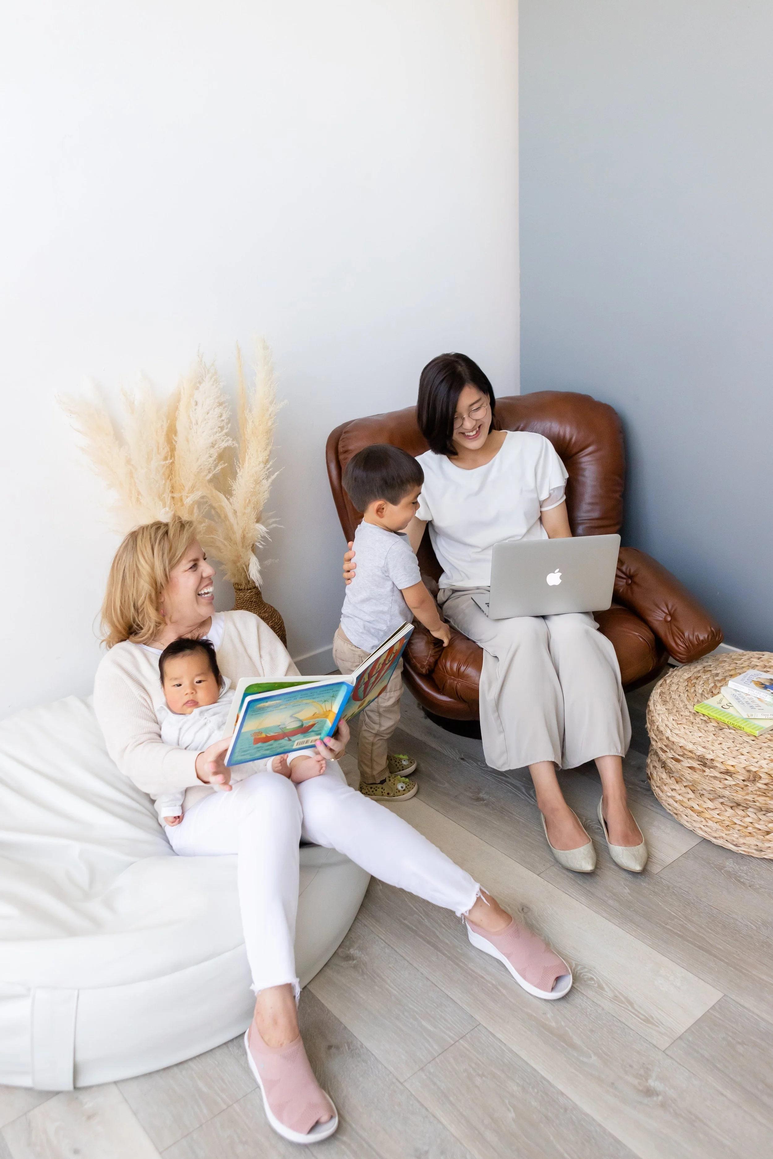 Nanny in Salt Lake City caring for a baby beside toddler while mother works in living room