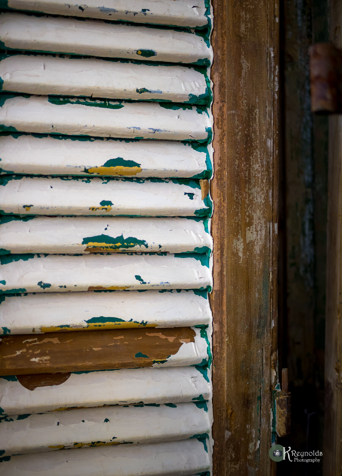 Close-up view of a weathered white metal vent cover with peeling paint, mounted on a worn wooden surface.