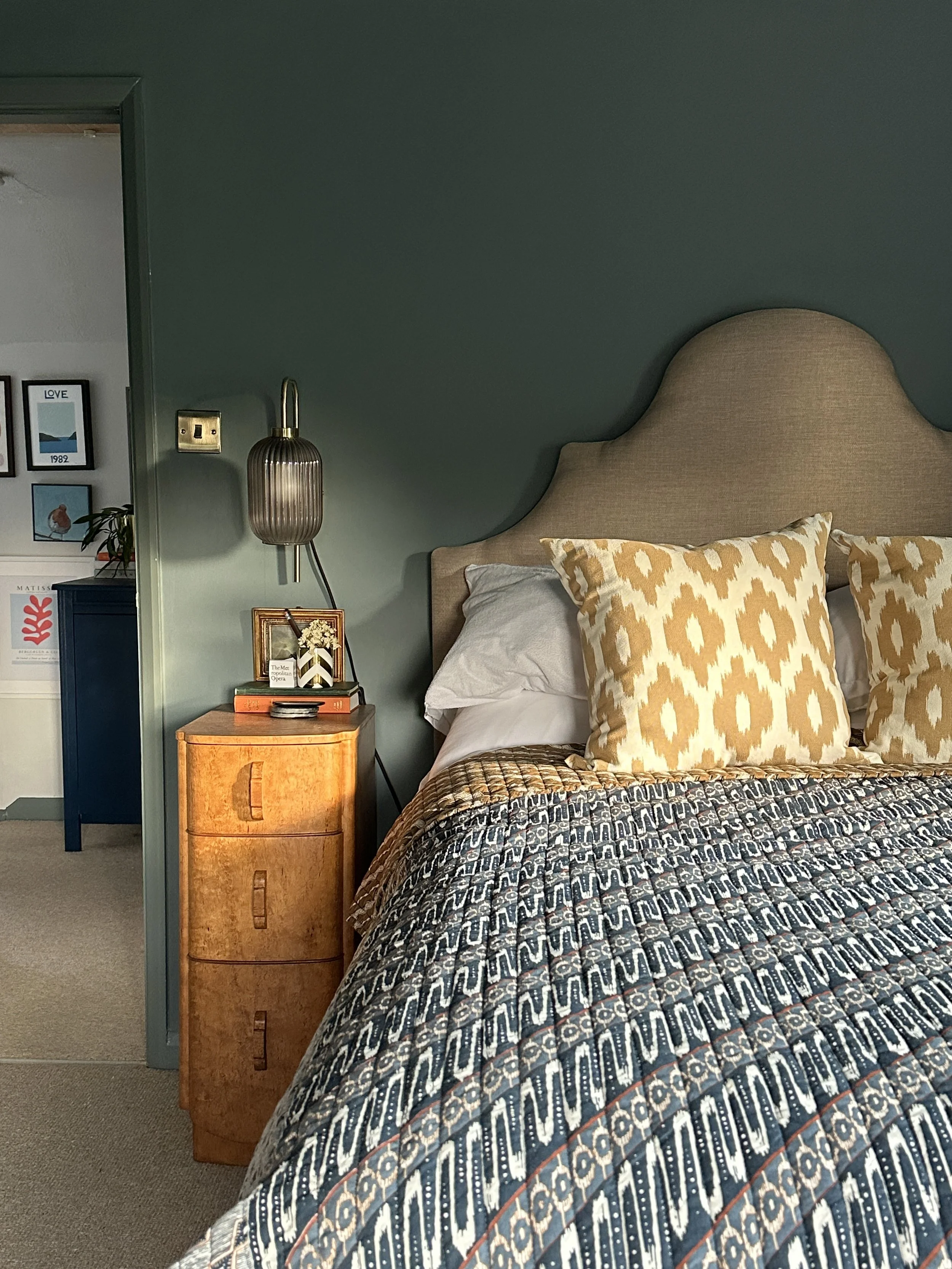 Upholstered headboard, patterned cushions and bedside table against the blue green walls.