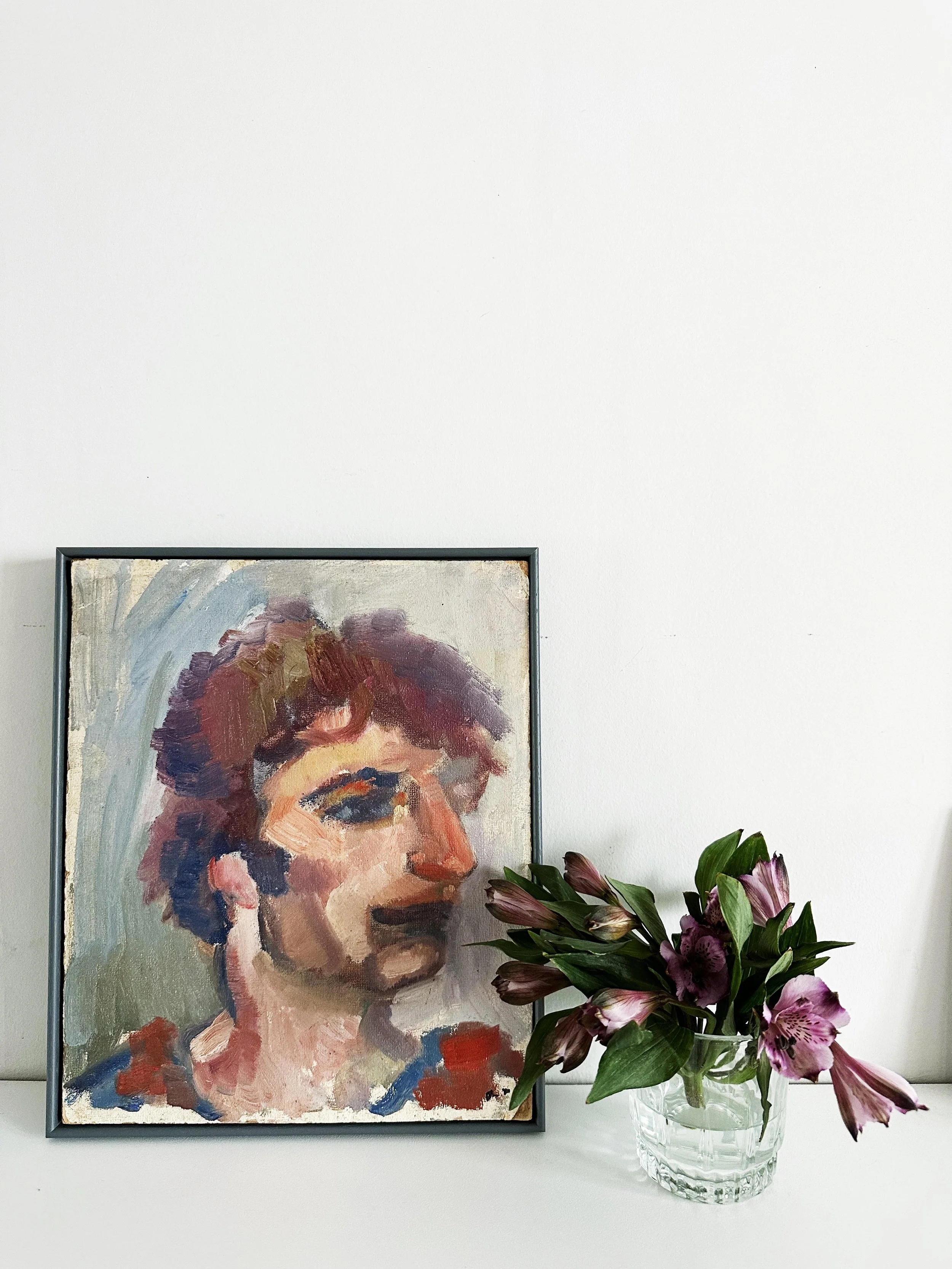 Vintage artwork against a plain wall, with a glass with cut flowers.