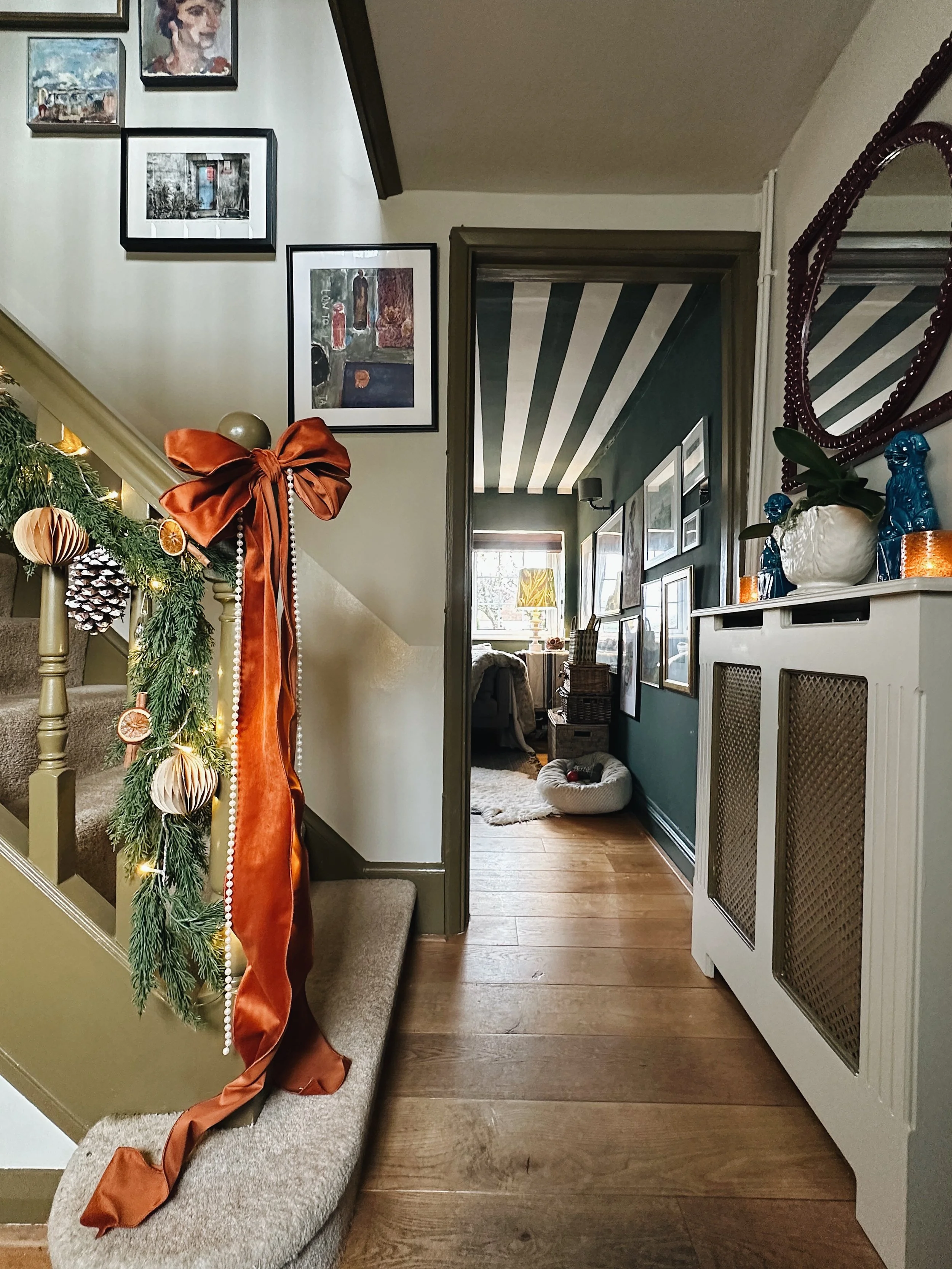 Victorian cottage hallway at Christmas with striped wall detailing, staircase garland and period character features.