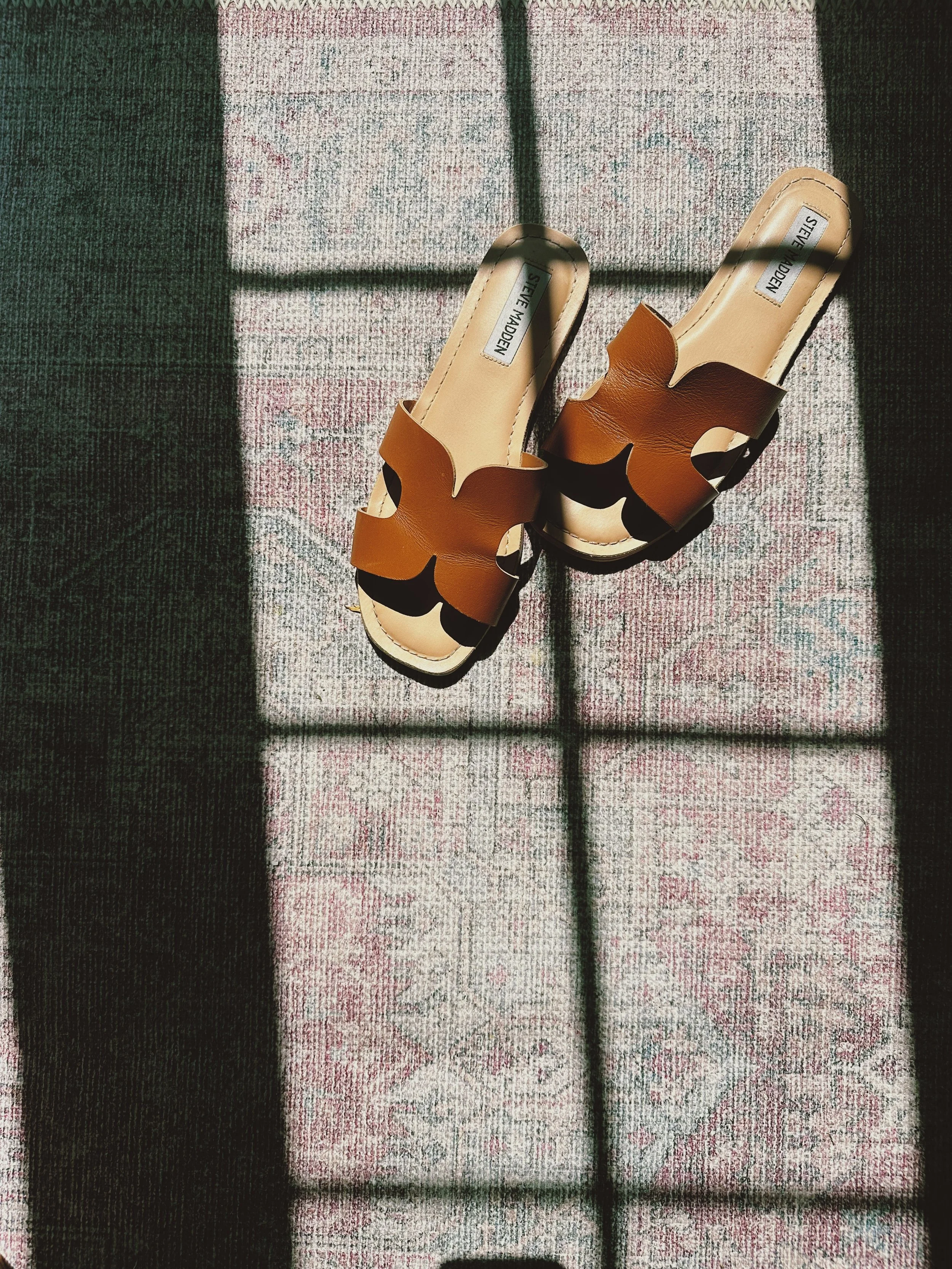 Leather sandals resting on a patterned runner illuminated by natural light.