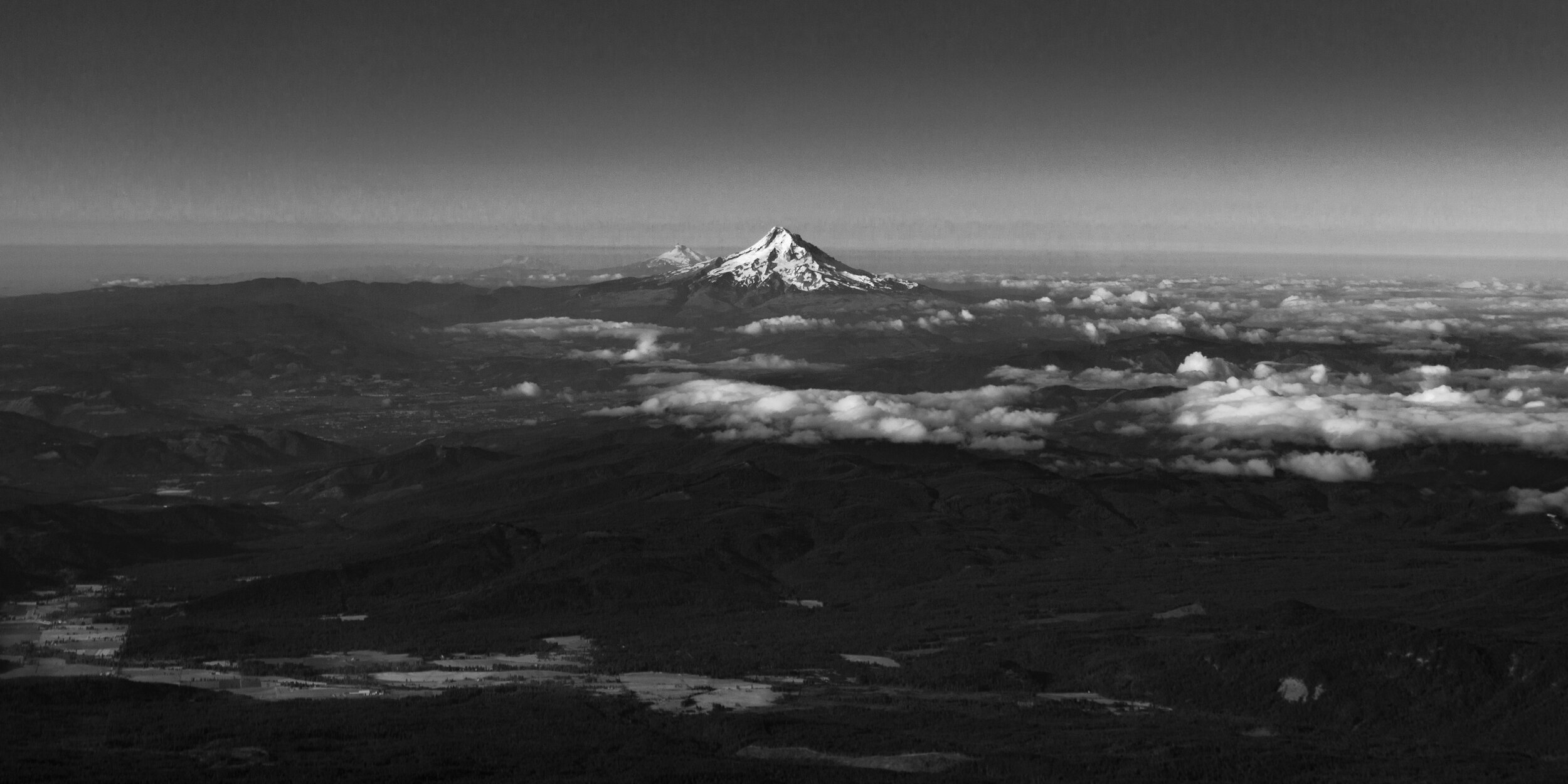 Black and white photo of a mountain landscape with snow-capped peaks and clouds below the mountains.