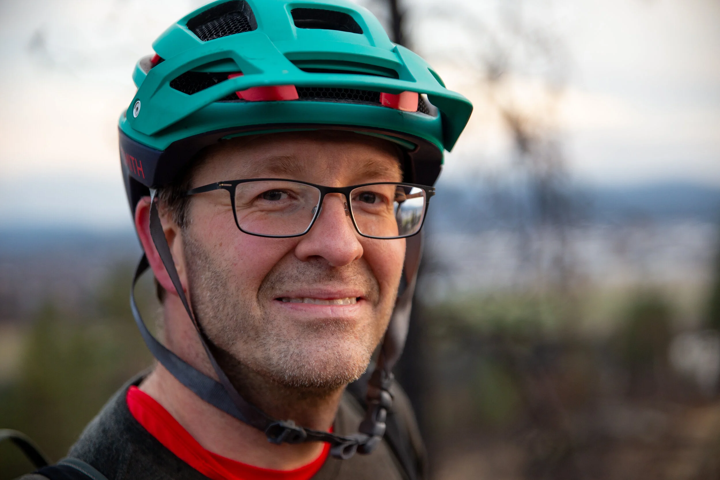 A man wearing glasses and a teal bicycle helmet outdoors.