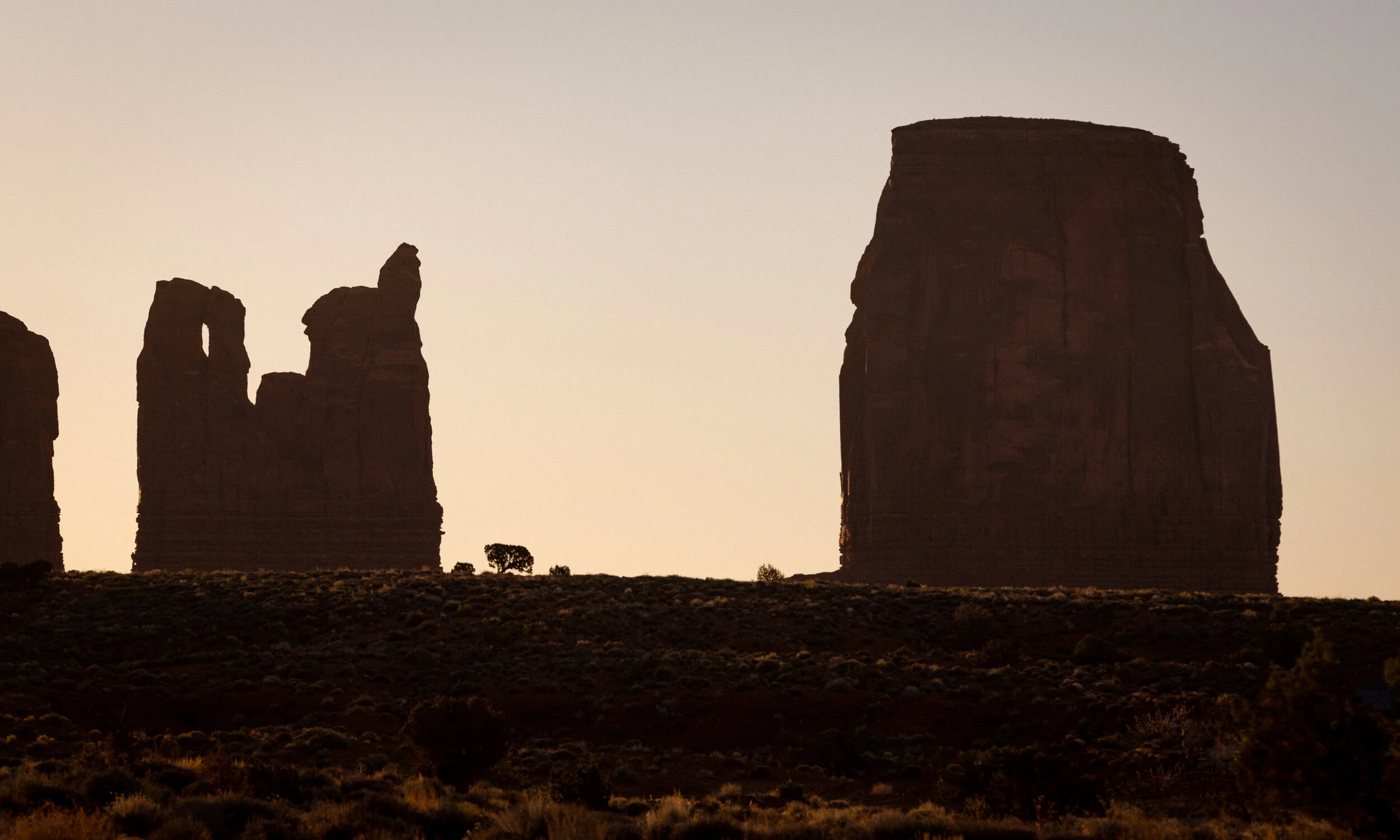 Silhouette of large rock formations in a desert landscape during sunset or sunrise.