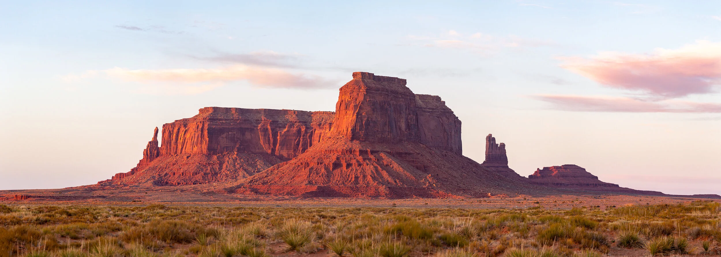 Sunset over the red rock formations of Monument Valley, with a partly cloudy sky.