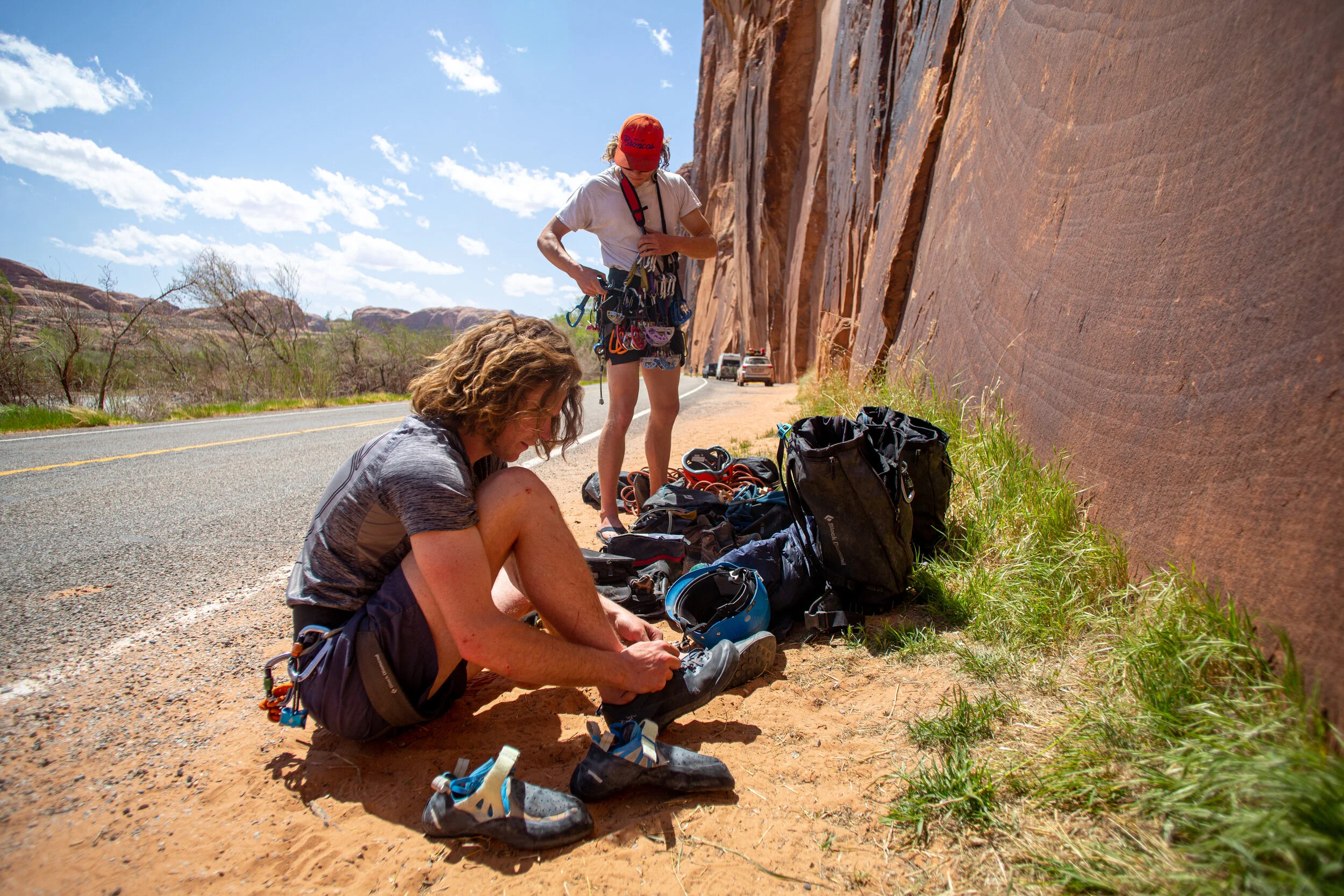 Two climbers are preparing gear on the roadside near the red rock formation in the Moab desert