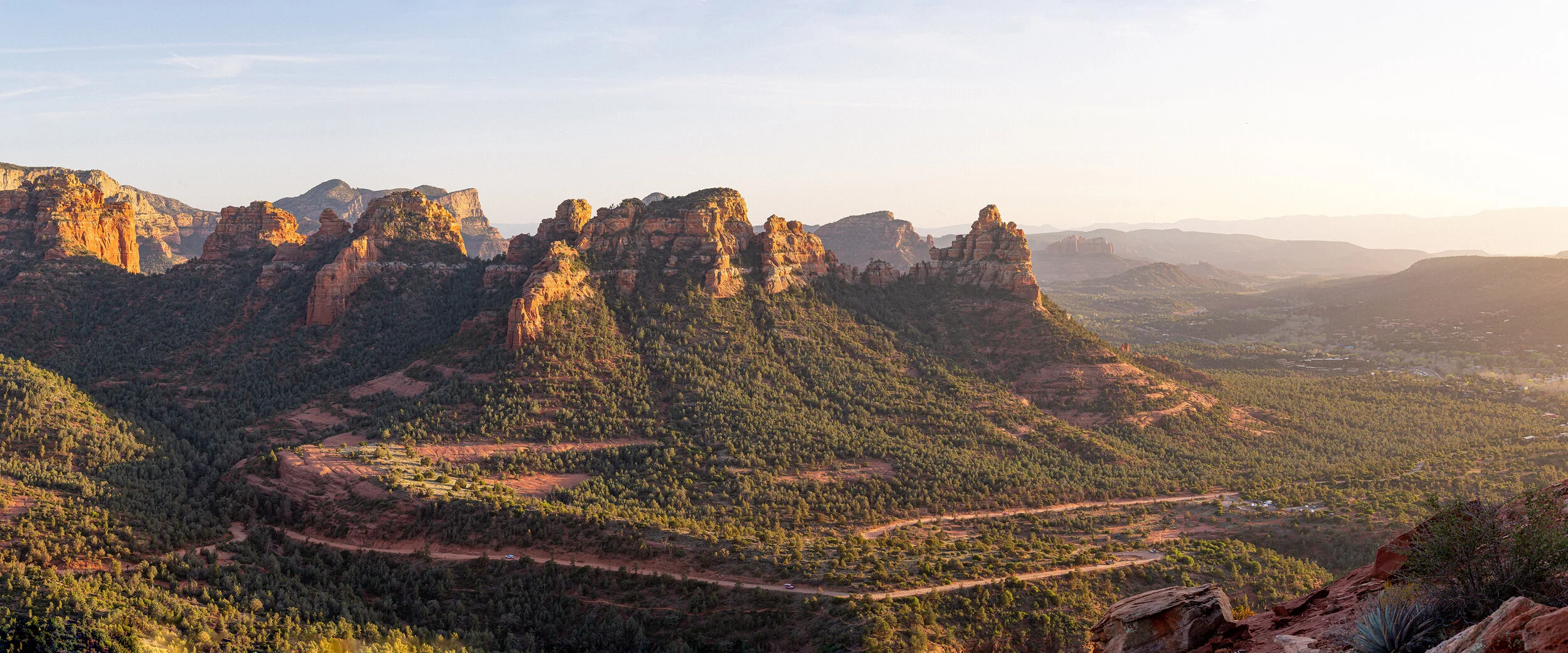 Sunset over red sandstone mountains with green vegetation in a desert landscape.
