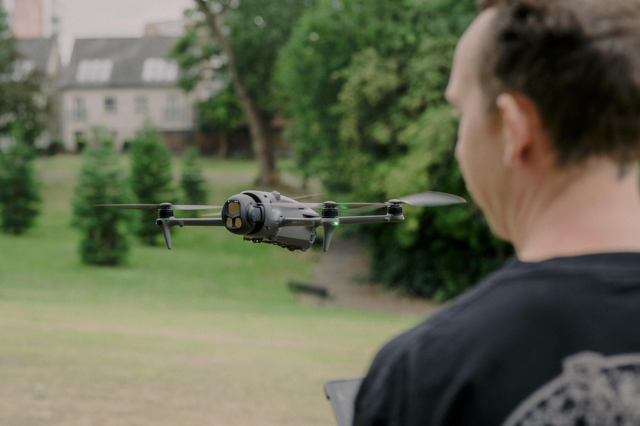 A person operating a drone outdoors in a park with green trees and grass.