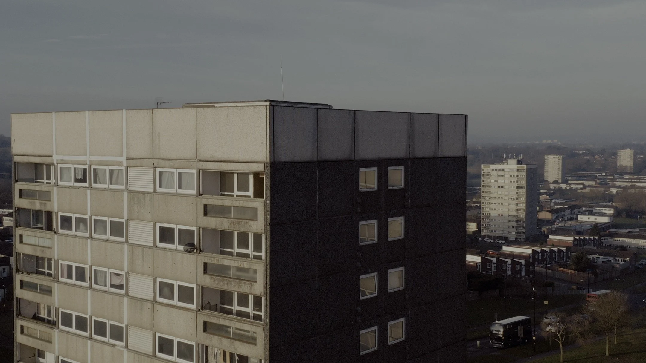 High-rise apartment building with beige and black exterior, many windows and balconies, with a cityscape in the background
