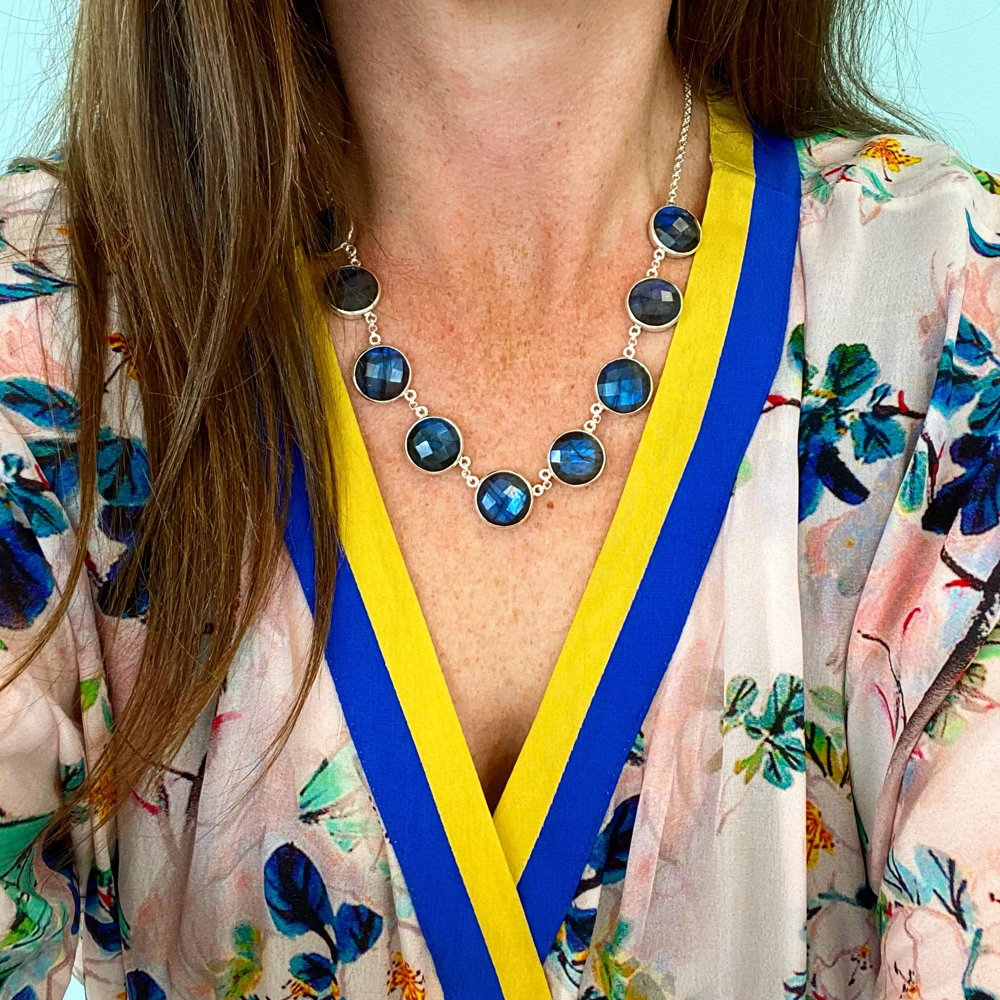 A woman wearing a floral top with a yellow and blue border, a silver necklace with blue circular stones.