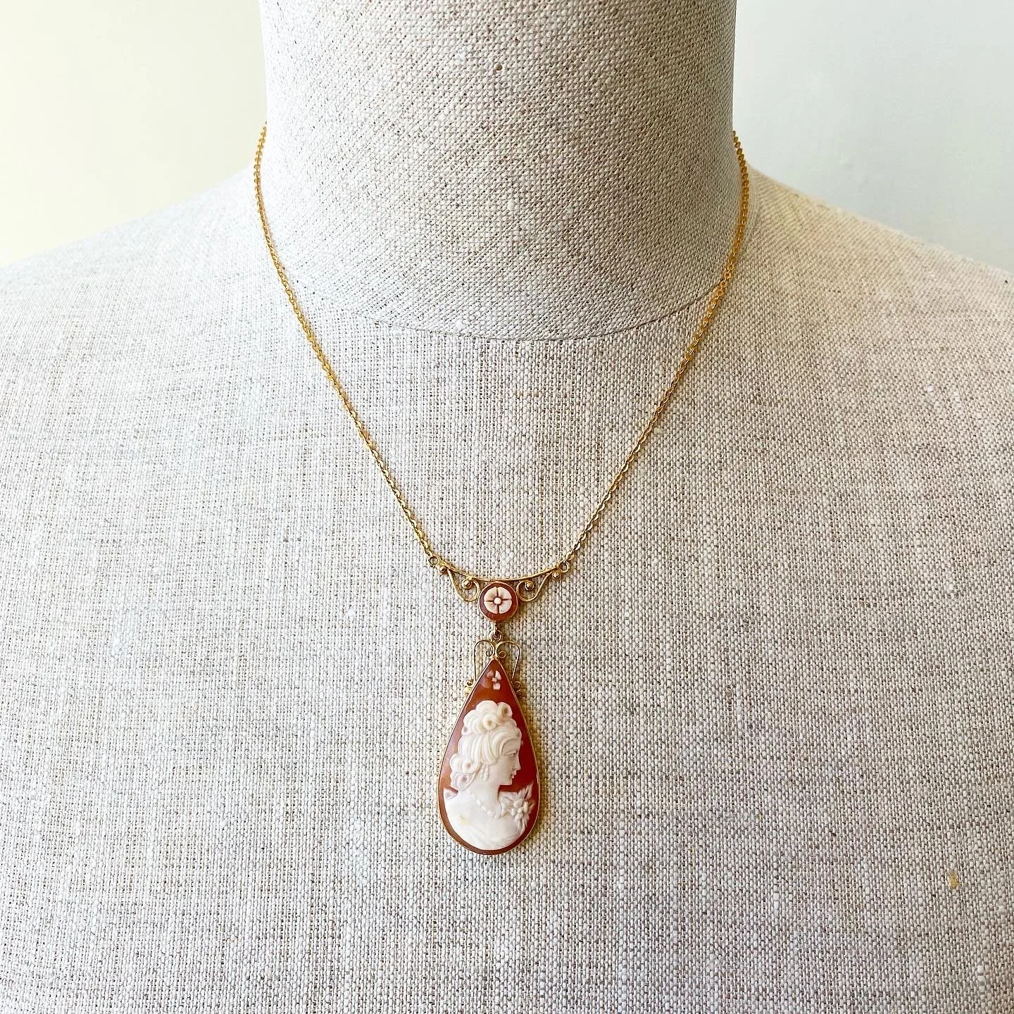 A necklace with a cameo pendant depicting a woman's profile, displayed on a fabric-covered display bust.