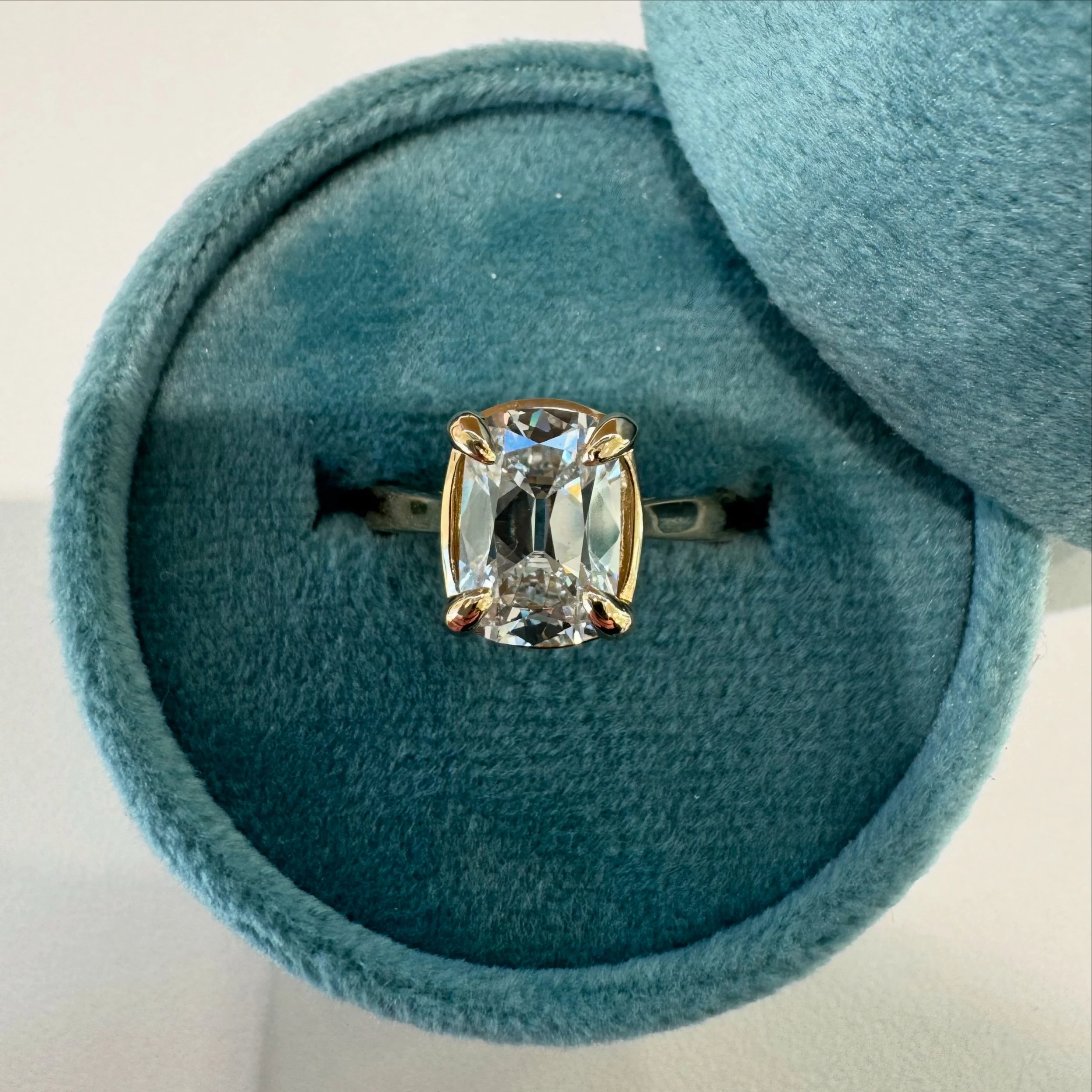 A ring with a large rectangular diamond in a gold setting inside a teal velvet jewelry box.