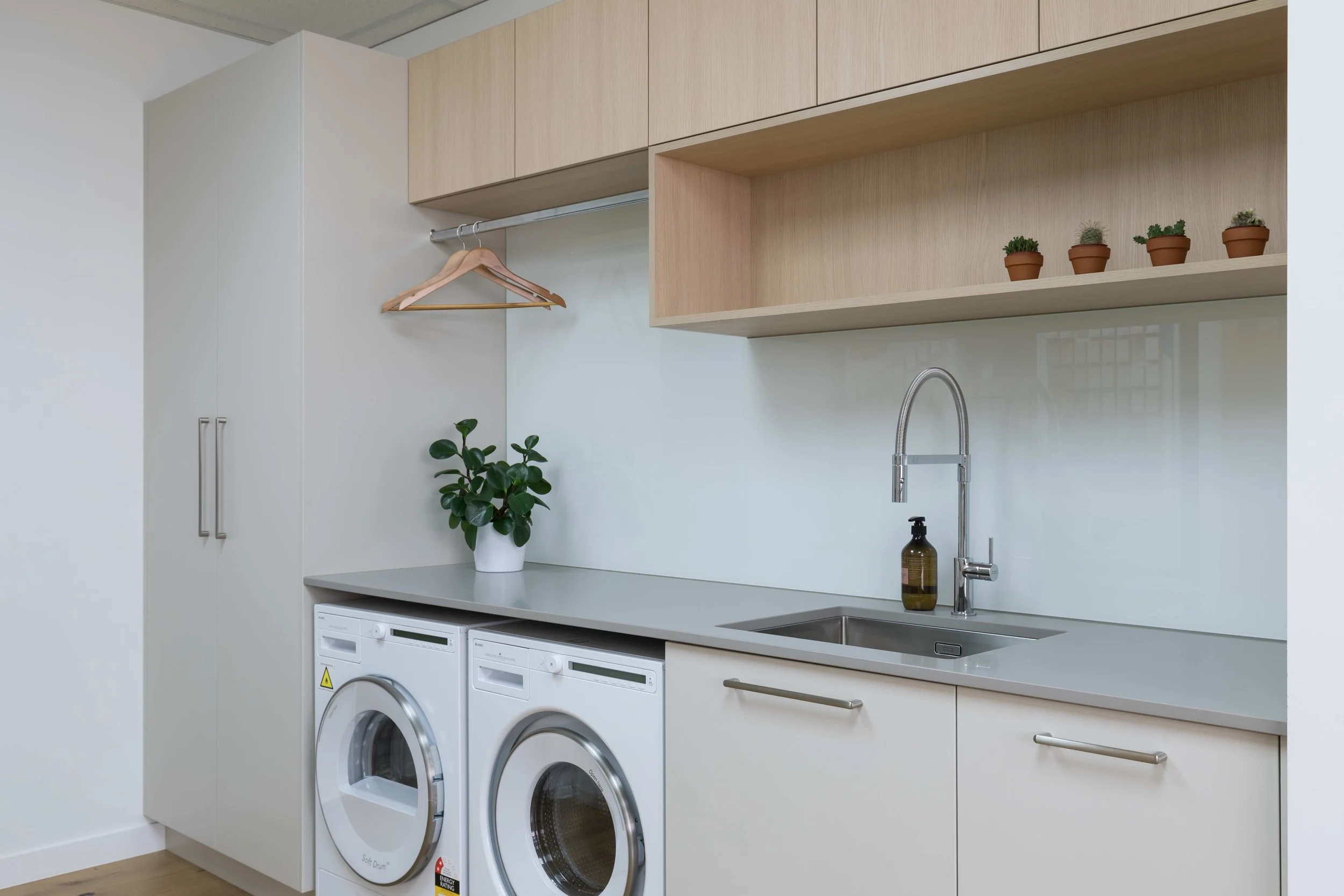 Laundry room with washer and dryer, countertop, sink with faucet, potted plant, and small potted succulents on shelf