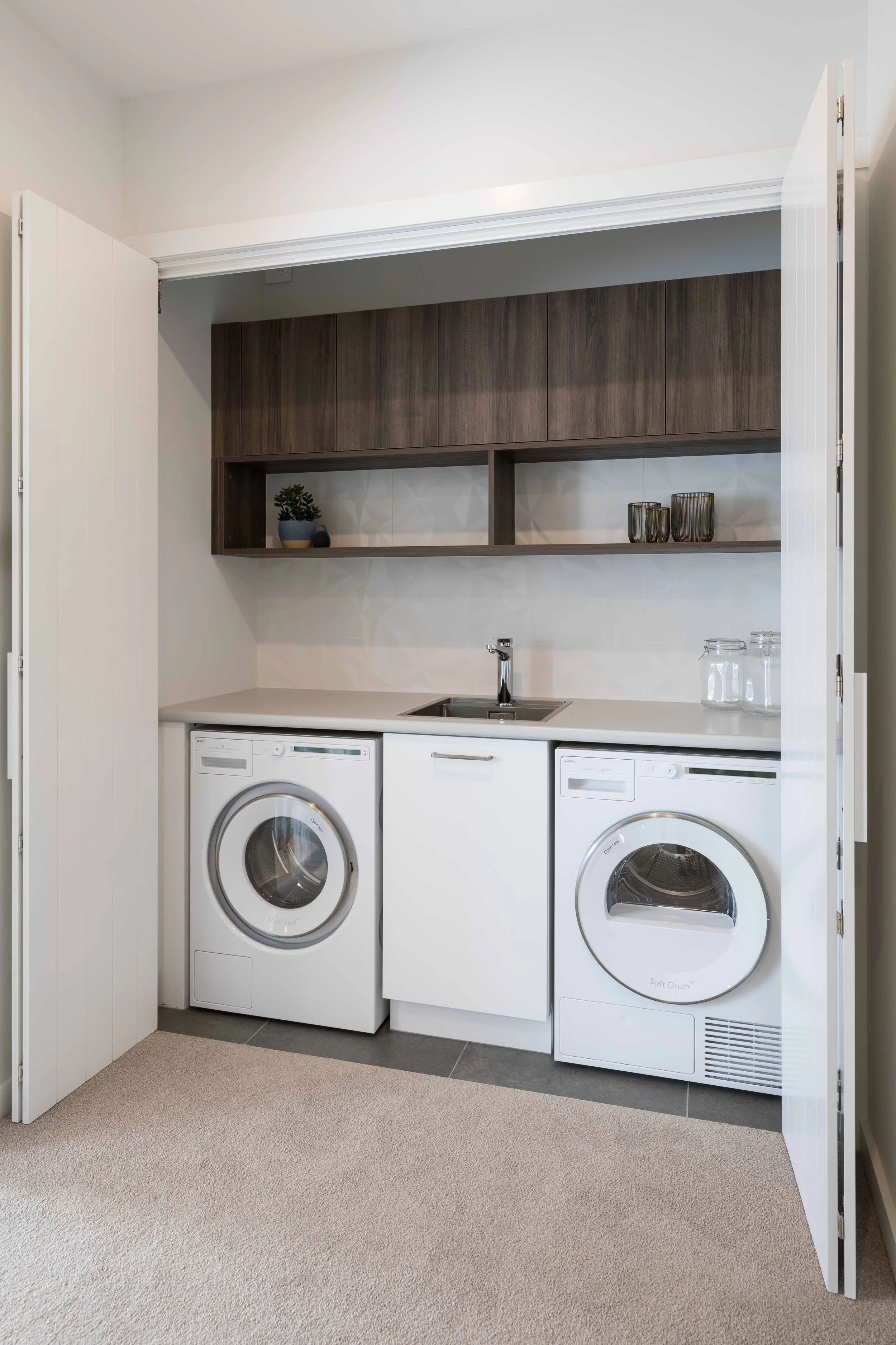 Laundry area with a washer, dryer, countertop, sink, and wall-mounted cabinets.