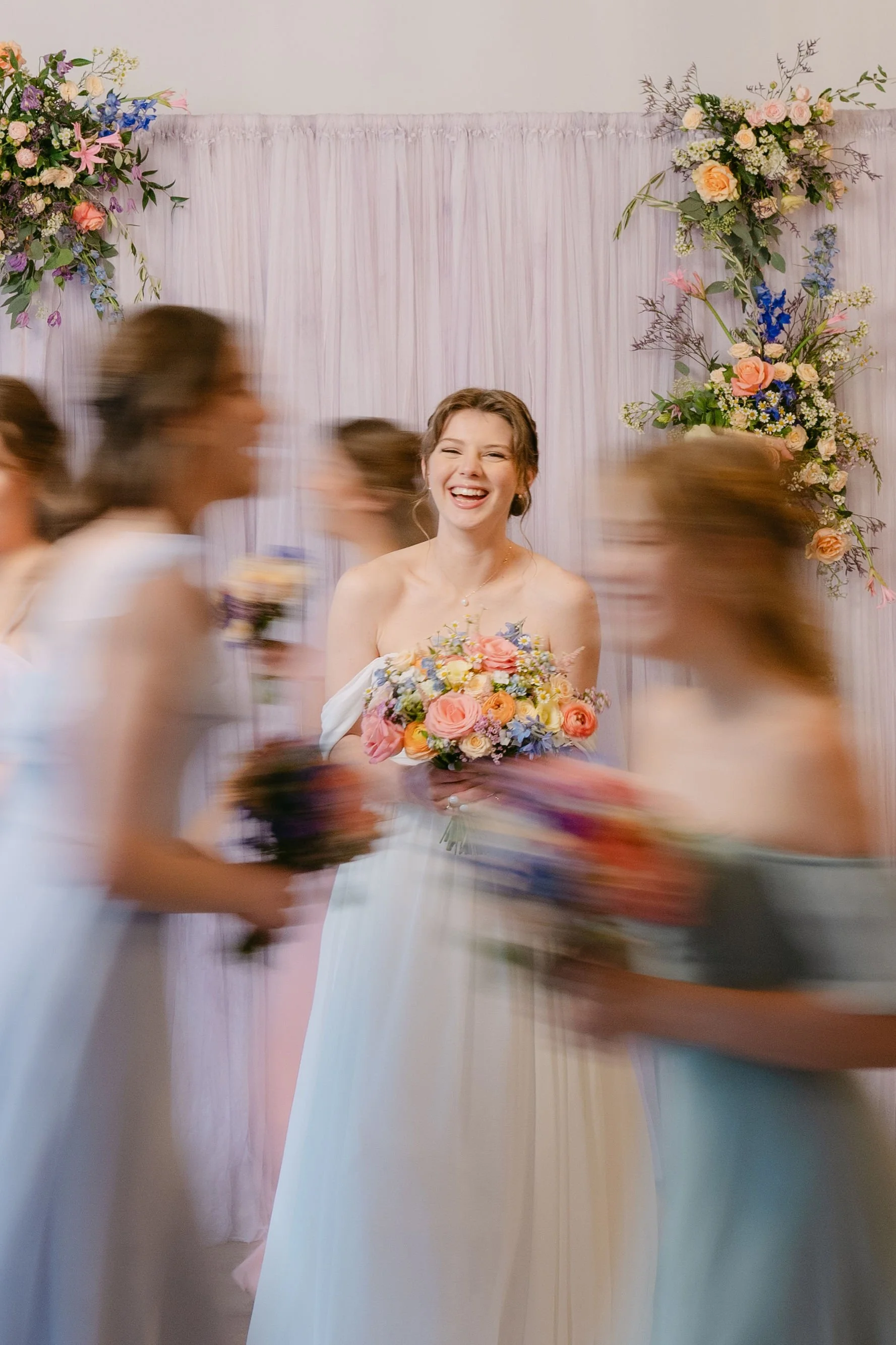 bride smiling holding spring florals with a purple hand-dyed tapestry from The Lovli Collection behind her