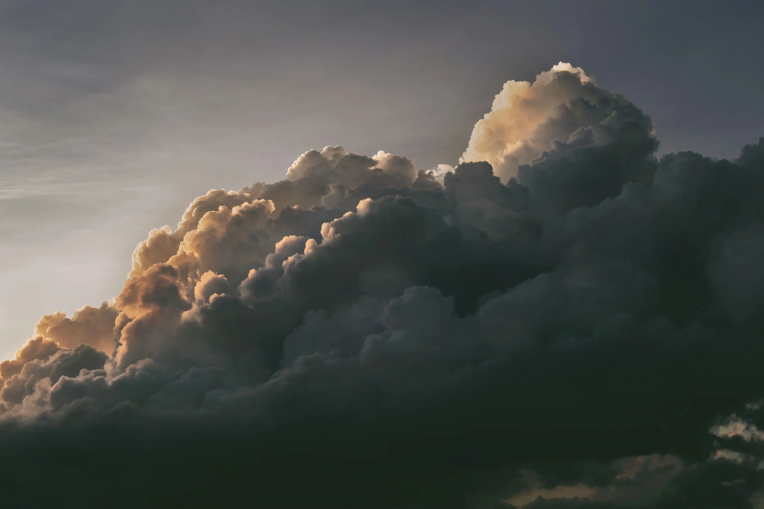 Dark, dense clouds in the sky with hints of sunlight illuminating their edges.