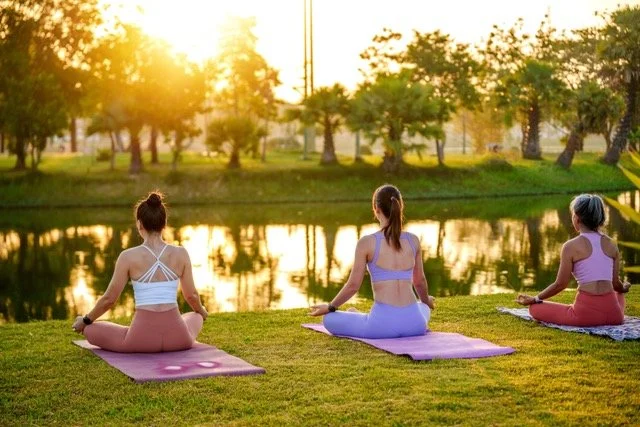 Women practising yoga on a mat outside in a park in Autumn