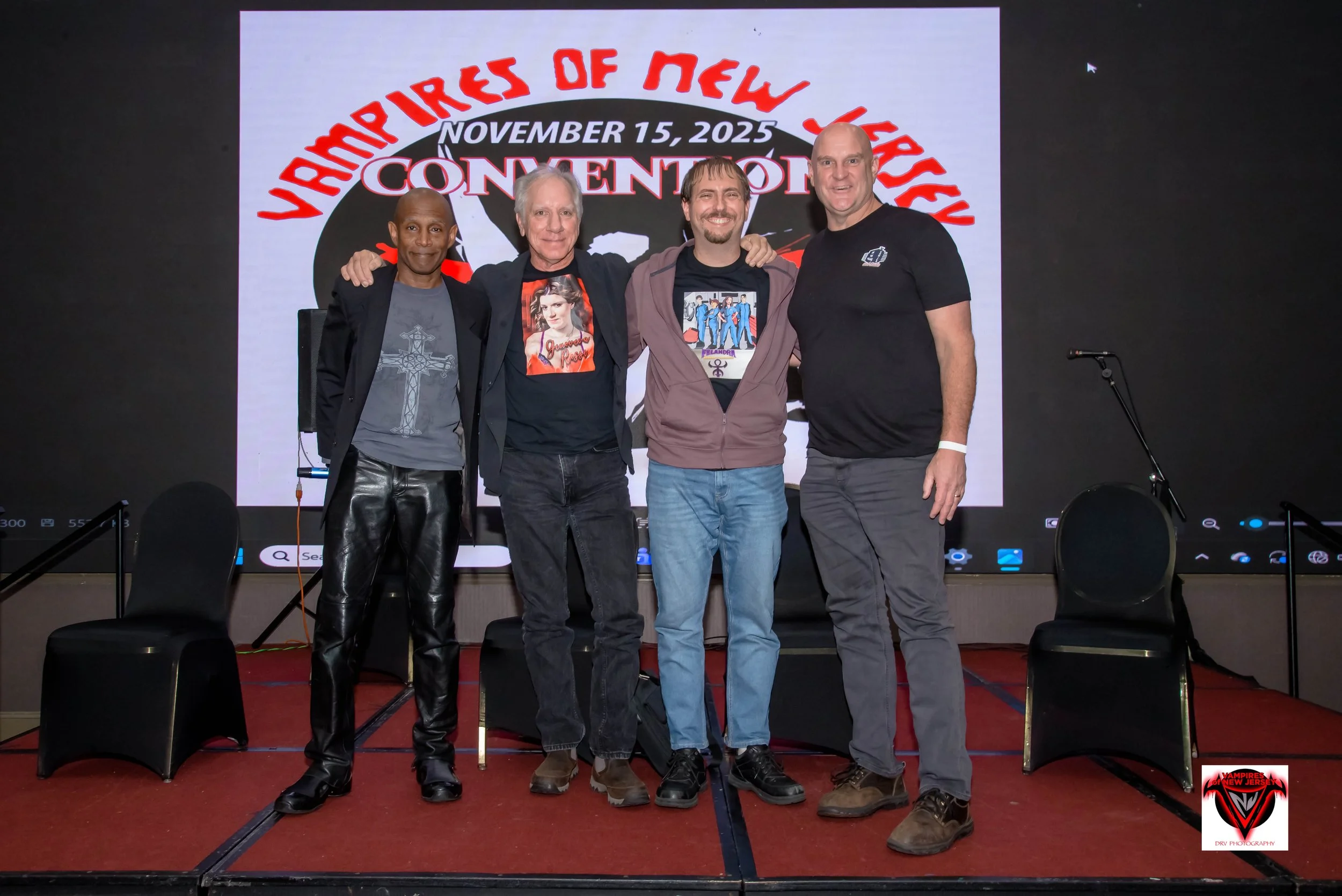 Jay Taylor, Blake Zdawski, and Alton Simpson standing on a stage with a large screen behind them, displaying 'Vampires of New Jersey Convention' and the date November 15, 2025. T