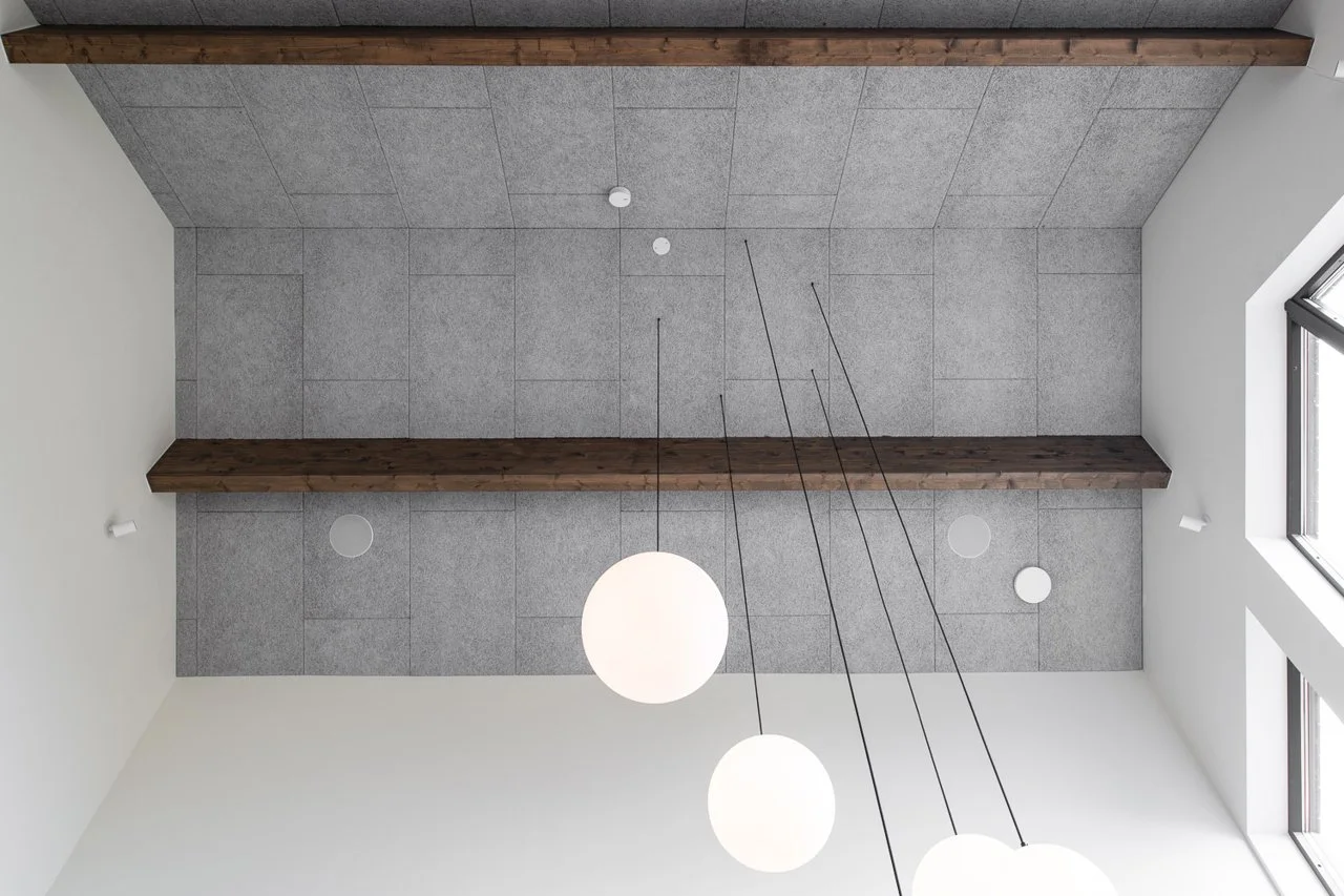 A modern interior ceiling with wooden beams, gray tiles, four spherical pendant lights, and a window on the side.