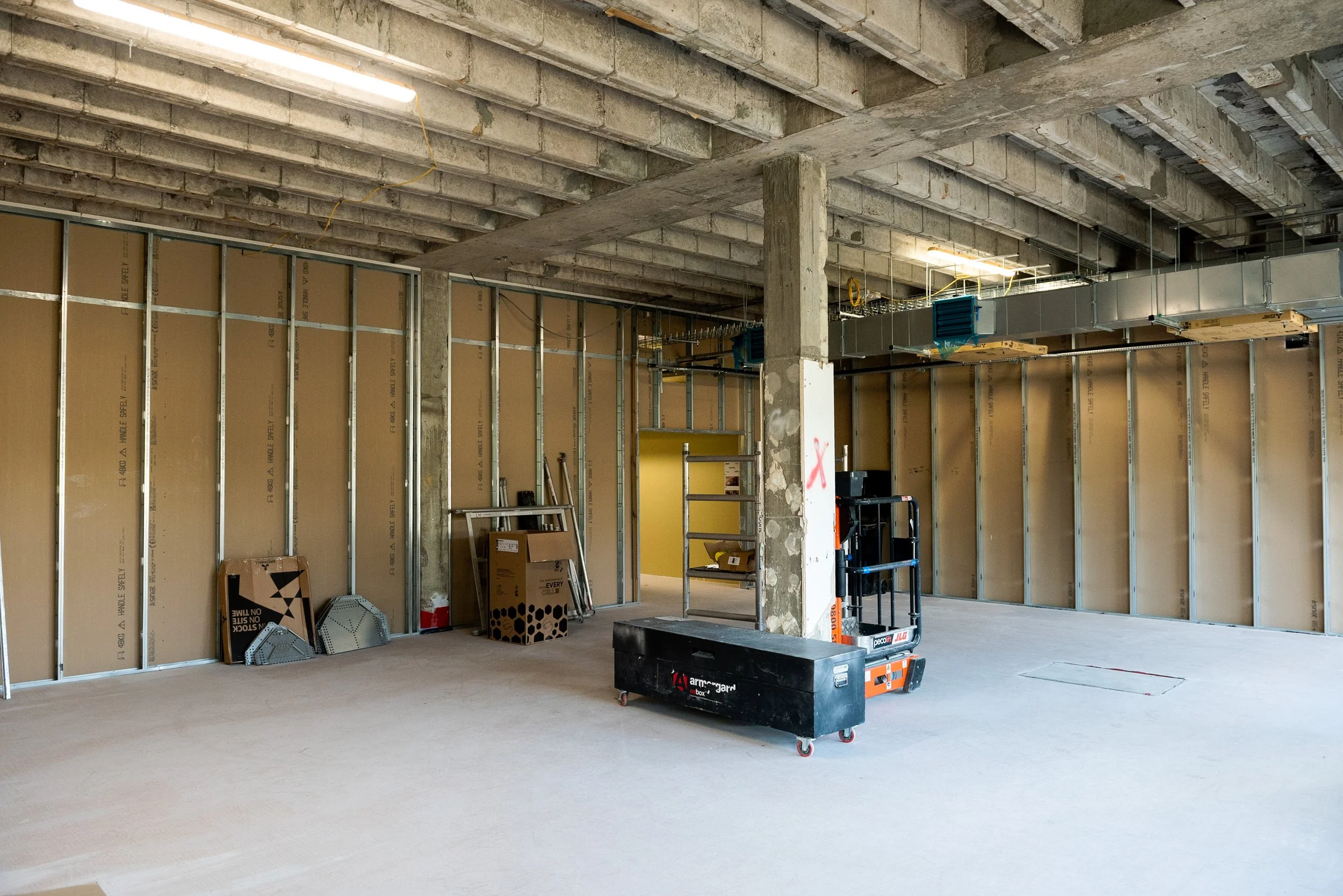 Metal stud framework and boarding in progress, with a scissor lift for overhead services and deflection heads