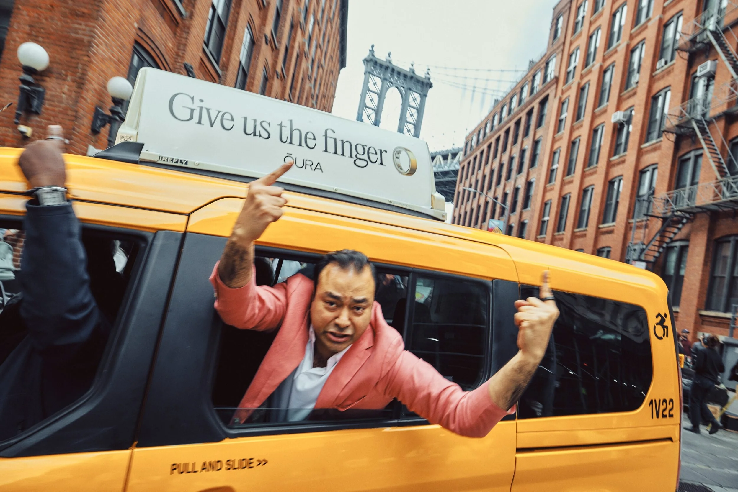 Yellow NYC taxi with a Firefly taxi top reading Give us the finger for ŌURA, passenger pointing upward
