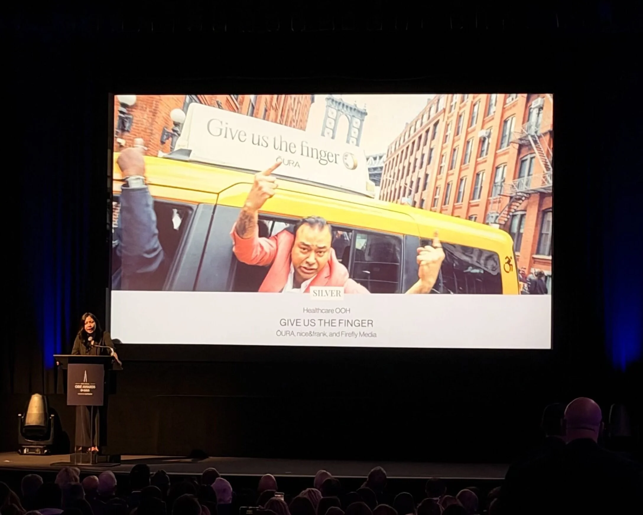 2026 OBIE Awards ceremony at MoMA, stage screen showing the Give Us the Finger campaign for ŌURA