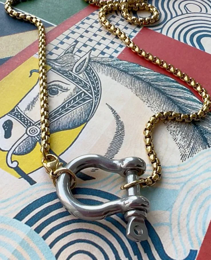 A gold chain necklace with a silver clasp shaped like a horseshoe, resting on a colorful paper surface with abstract patterns and illustrations.