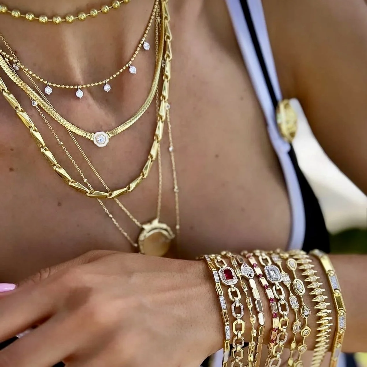 A woman wearing multiple gold necklaces and bracelets, with a black and white outfit and a gold watch.
