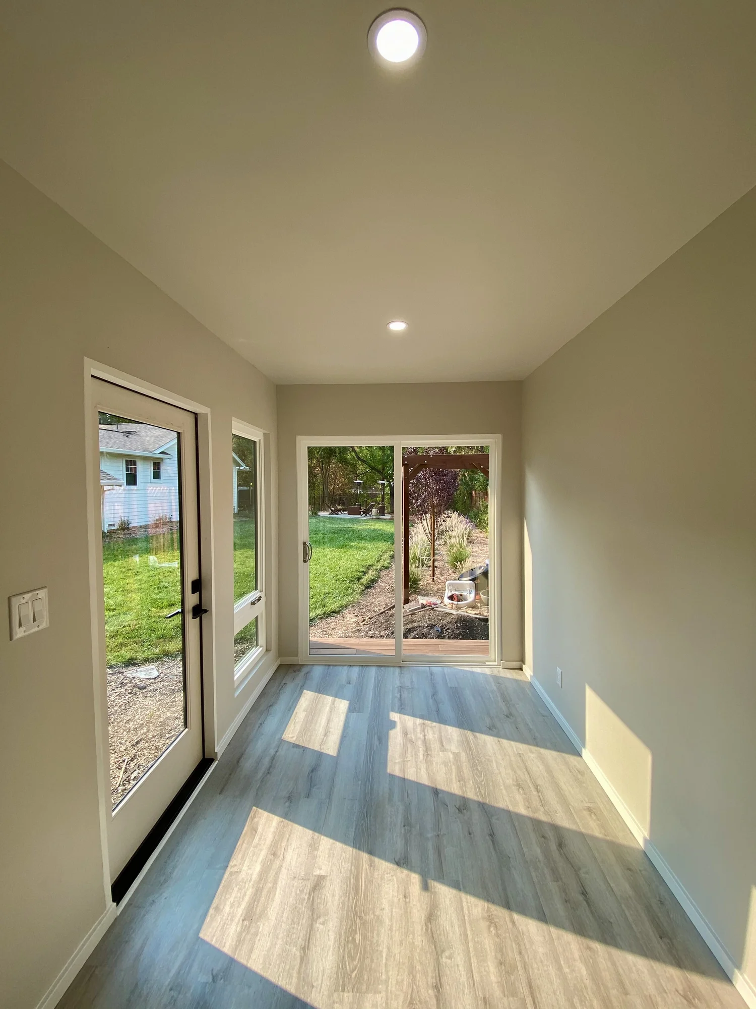 Empty finished interior of a Bay Modular studio with light wood-look floors, recessed ceiling lights, and glass doors at both ends