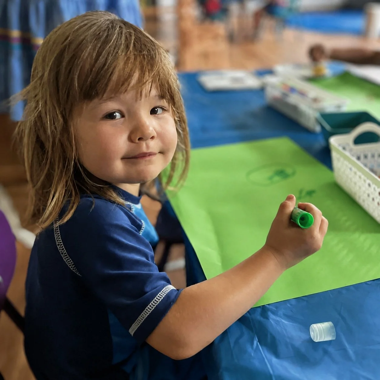 A smiling child coloring on a piece of green paper.
