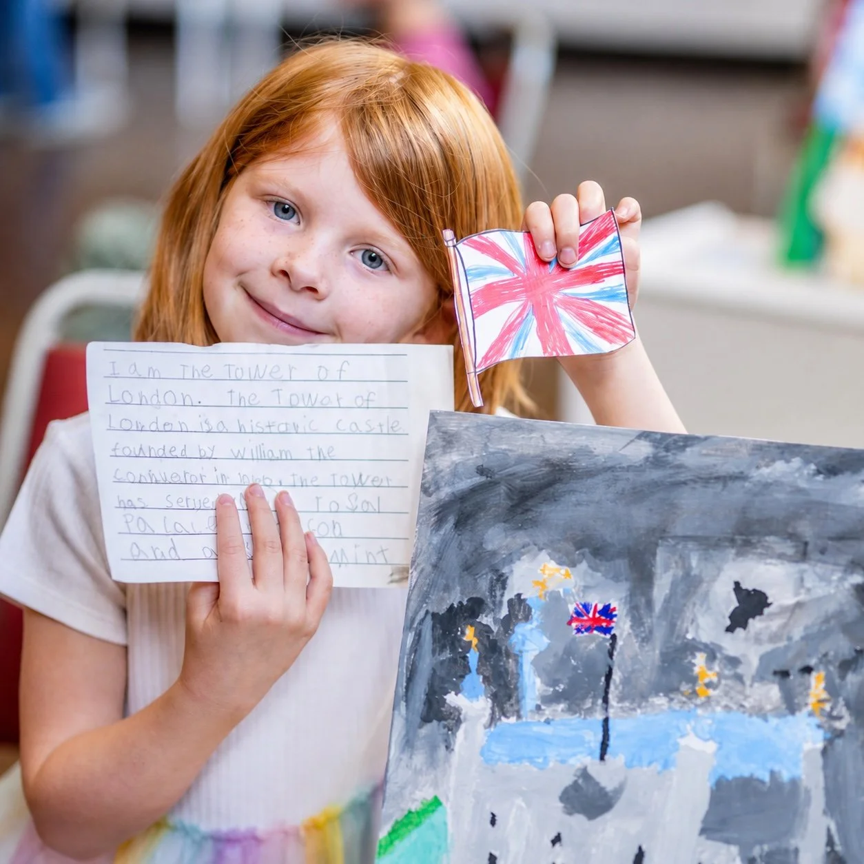 A child holding up a hand-written note next to a painting.