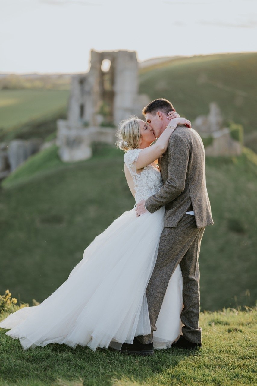  bride and groom who got married at corfe castle in Dorset kissing with the castle in the backdrop 
