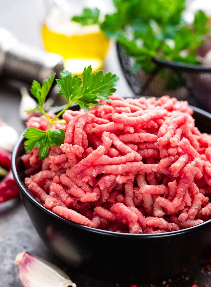 Ground beef in a black bowl garnished with parsley, with a lemon slice and fresh herbs in the background.