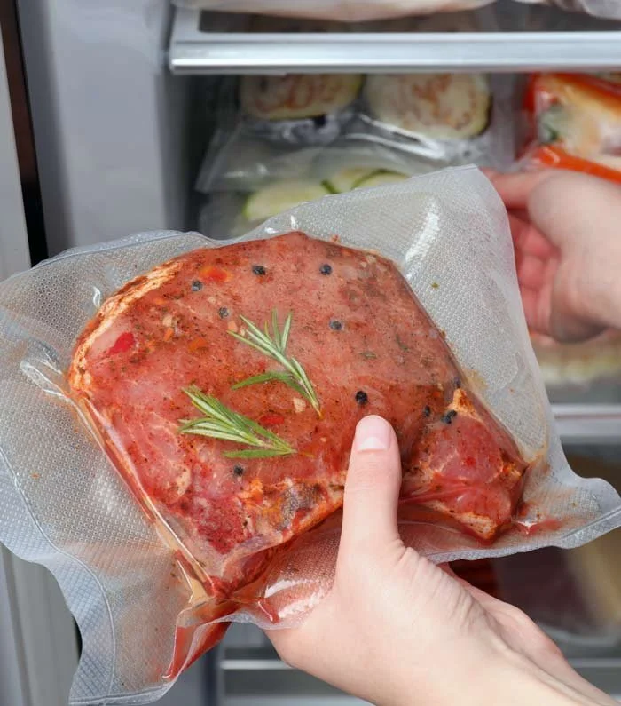 Raw seasoned meat portion sealed in vacuum bag, garnished with fresh rosemary.